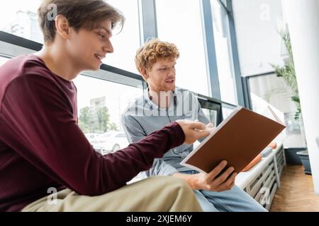 Due giovani seduti su una panchina, ingrossati in un libro. Foto Stock