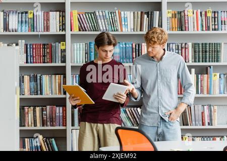 Due studenti maschi coinvolti in un libro in una biblioteca. Foto Stock