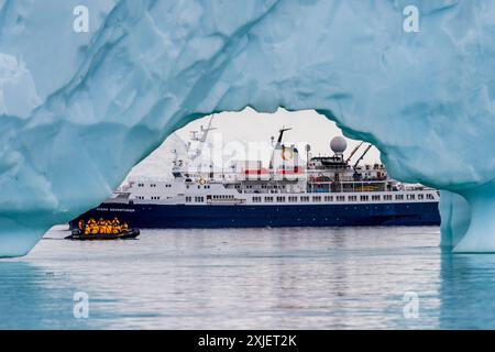 Isola di Cuverville, Penisola Antartica - 31 gennaio 2024. Nave da spedizione antartica l'avventuriero oceanico è ancorata vicino all'isola di Cuverville sulla penisola antartica e incorniciata da un iceberg in primo piano. Foto Stock