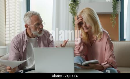 Arrabbiato turbato 50s sposato anziano anziano Caucasico coppia donna uomo maturo uomini uomini uomini d'affari famiglia fallimento documenti aziendali carta laptop Foto Stock