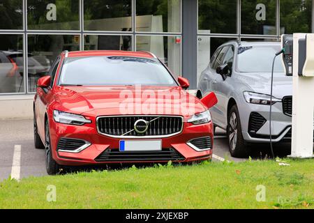 Auto elettrica ibrida rossa Volvo V60 (II) AWD 2024 collegata al caricabatteria presso la concessionaria accanto a Volvo XC60 PHEV. Salo, Finlandia 14 luglio 2024. Foto Stock