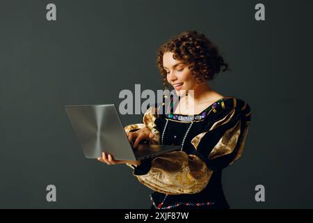 Ritratto di una giovane donna aristocratica vestita con un abito medievale che lavora su un computer portatile Foto Stock