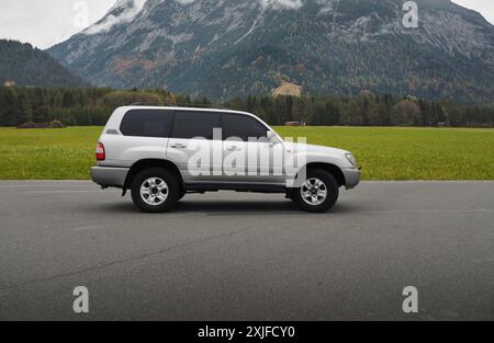 Toyota Land Cruiser silver nel parcheggio nella campagna alpina. Vista laterale del SUV degli anni '1990 di fronte a una montagna in una giornata nuvolosa. Foto Stock