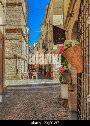 ALGHERO, ITALIA - 4 LUGLIO 2024: Pittoresca strada medievale tipica sarda con piccoli ristoranti tradizionali. Foto Stock