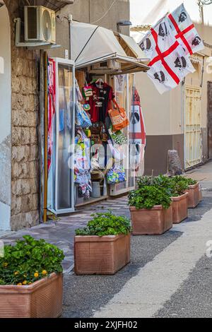 ALGHERO, ITALIA - 4 LUGLIO 2024: Pittoresca strada medievale, tipica sarda, con un piccolo negozio di souvenir tradizionale. La bandiera della provincia di Sardi Foto Stock