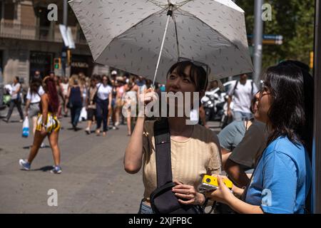 Barcellona, Spagna. 18 luglio 2024. Una turista asiatica si è vista coprirsi dal sole con un ombrello mentre ammirava un edificio unico del modernismo catalano. La prima ondata di caldo dell'estate presenta avvisi di avvertimento in alcune regioni della Spagna. Temperature superiori a 40 gradi sono attese nella maggior parte delle regioni della Spagna meridionale. La città di Barcellona sta già vivendo un forte aumento del calore, soprattutto nelle aree aperte senza ombra. (Foto di Paco Freire/SOPA Images/Sipa USA) credito: SIPA USA/Alamy Live News Foto Stock