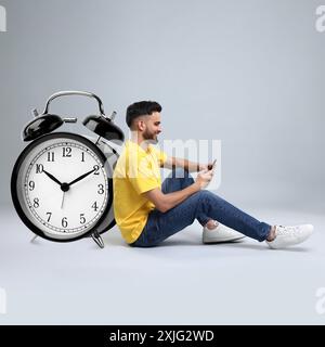 Uomo con smartphone e grande sveglia su sfondo grigio Foto Stock