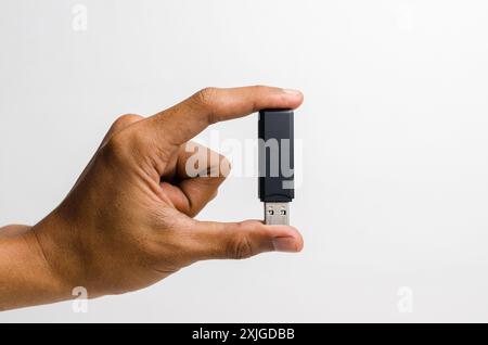 Mano di un uomo che tiene in mano un'unità flash USB nera con la punta delle dita, isolata su sfondo bianco. Foto Stock