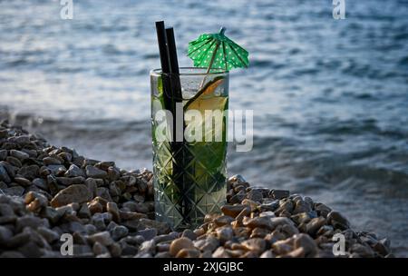 Un bicchiere di cocktail mojito rinfrescante e' in piedi sulle rocce in riva al mare. Foto Stock