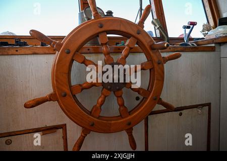 La ruota in legno lucidato montata sul ponte di un'imbarcazione a vela controlla lo sterzo. Foto Stock