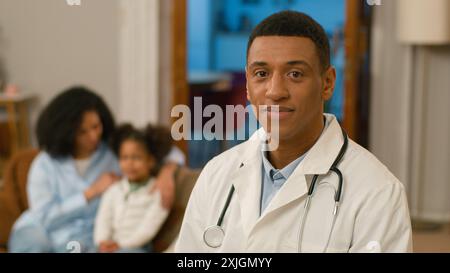 Afroamericano uomo medico che guarda la macchina fotografica sorridente logopedista pediatra casa chiamare operatore sanitario famiglia madre e figlia aiuto Foto Stock