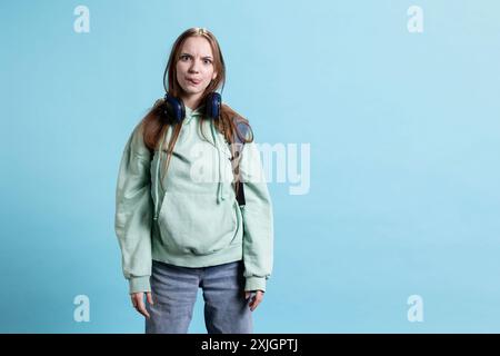 Giovane ragazza che si mette la lingua fuori, fa strane espressioni facciali, isolata sullo sfondo dello studio. Adolescente che fa facce sciocche, si diverte a recitare zany, ad essere espressiva Foto Stock