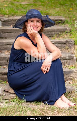 Una donna di 50-55 anni con un vestito blu siede su gradini di pietra Foto Stock