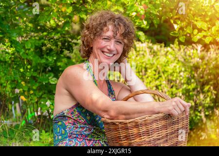 Donna che sorride con un cesto in un giardino Foto Stock