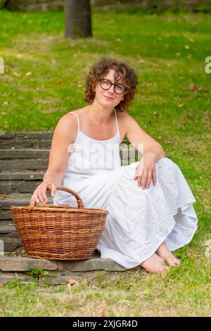 Donna con abito bianco seduta su gradini di pietra con cestino in vimini Foto Stock