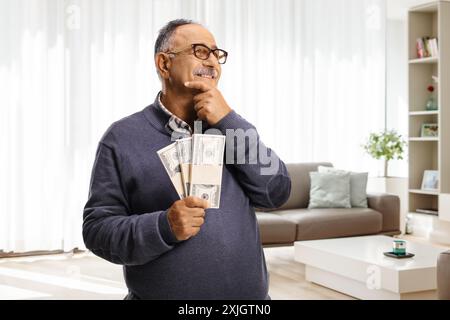 Uomo maturo felice che tiene i soldi e pensa a casa in salotto Foto Stock