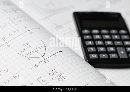 Copybook con formule matematiche scritte a mano e calcolatrice come sfondo, primo piano Foto Stock