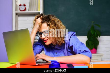 Insegnante di scuola o tutor universitaria seduto alla scrivania in classe. Torna a scuola. L'insegnante universitario lavora con un computer portatile. Studentessa che si sta preparando Foto Stock