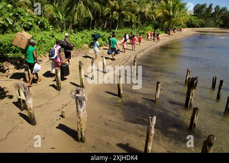 Gli abitanti del villaggio trasportano i bagagli dei turisti che arrivano in barca, mentre camminano lungo la spiaggia nel villaggio di Horale, Seram, Maluku centrale, Maluku, Indonesia. Foto Stock