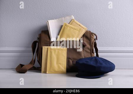 Borsone, buste, giornali e cappello marroni vicino alla parete grigia Foto Stock