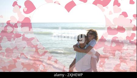 Immagine di cuori che si muovono su un uomo birazziale che trasporta una donna in spiaggia in estate Foto Stock