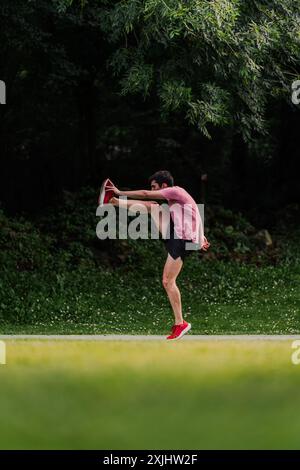 Giovane che solleva le gambe per riscaldarsi prima di andare a correre. Verticale Foto Stock