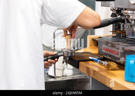 Il barista sta sta tamponando il caffè con una manomissione nel cestello del portafiltro Foto Stock