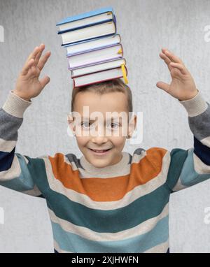 allegro bambino di 8 anni ha una pila di libri sulla testa. torna a scuola. Prenota giorno. Legga con piacere. concetto di lettura, istruzione, saggezza, conoscenza Foto Stock