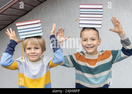 Due fratelli o amici per 7 anni bilanciano pile di libri sulla loro testa. felice incontro di compagni di classe, di nuovo a scuola. Prenota giorno. concetto di lettura Foto Stock