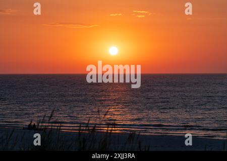 Splendido tramonto sul Mar Baltico. Lame d'erba sfocate in primo piano. Sagome di due persone sedute su una bella e ampia spiaggia e watchi Foto Stock