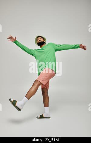 Il bell'uomo afroamericano indossa una camicia verde alla moda e pantaloncini rosa sullo sfondo vivace. Foto Stock