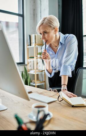 Una donna d'affari di mezza età con i capelli corti si siede a una scrivania, completamente concentrata sul suo laptop mentre lavora in ufficio. Foto Stock