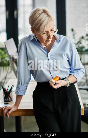 Una donna d'affari di mezza età con capelli corti vestiti con una camicia blu e pantaloni neri che reggono una bottiglia con pillole Foto Stock