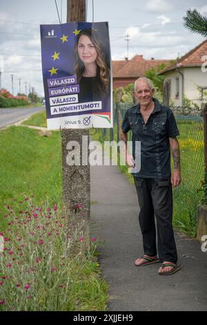 un uomo anziano in piedi accanto al manifesto dei candidati alle elezioni europee nel piccolo villaggio ungherese mentre va al seggio elettorale per esprimere il suo voto Foto Stock