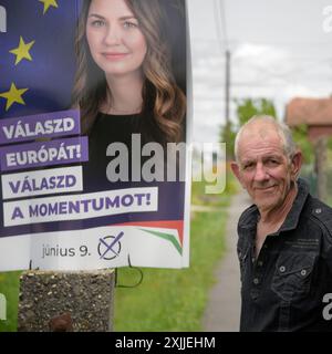 un uomo anziano in piedi accanto al manifesto dei candidati alle elezioni europee nel piccolo villaggio ungherese mentre va al seggio elettorale per esprimere il suo voto Foto Stock