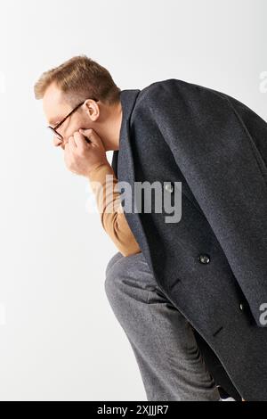 Un uomo elegante in tuta e occhiali si appoggia contro un muro. Foto Stock