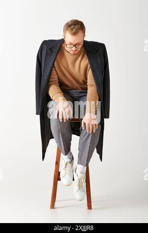 Un bell'uomo in un abbigliamento elegante posa attivamente mentre si siede su una sedia di legno. Foto Stock