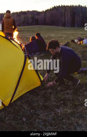 l'uomo prepara una tenda durante un viaggio in campeggio, tenda da da campeggio al tramonto. Foto Stock