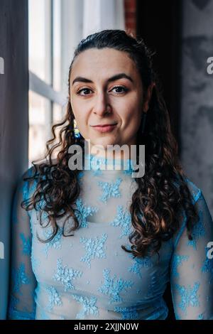 Donna sicura di sé in pizzo blu vicino a una finestra. Foto Stock