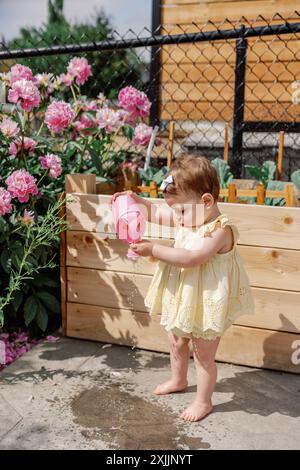 Bimbo che innaffia le piante in giardino, godendosi una giornata di sole Foto Stock