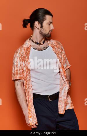 Bell'uomo caucasico con abbigliamento alla moda si erge con sicurezza contro una parete arancione brillante. Foto Stock