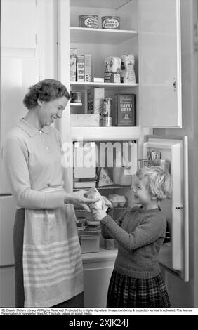 In cucina anni '1960 Una madre e una figlia nella sua cucina con la porta aperta sul frigorifero. Potete vedere i prodotti alimentari di vari tipi che sono ordinatamente esposti sugli scaffali. Tra le altre cose, il classico pacchetto di latte Tetran è visibile. Inventato da Erik Wallenberg, dipendente di Ruben Rausings, che divenne l'inizio dell'impero del packaging Tetra Pak. Svezia 1960. Conard rif. 4188 Foto Stock