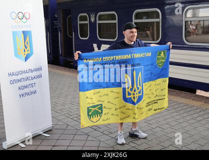 KIEV, UCRAINA - 18 LUGLIO 2024 - l'atleta Oleh Vierniaiev detiene una bandiera sulla piattaforma della stazione ferroviaria di Kiev-Pasazhyrskyi mentre la squadra di ginnastica artistica Ucraina parte per le Olimpiadi estive di Parigi 2024, Kiev, capitale dell'Ucraina. Foto Stock