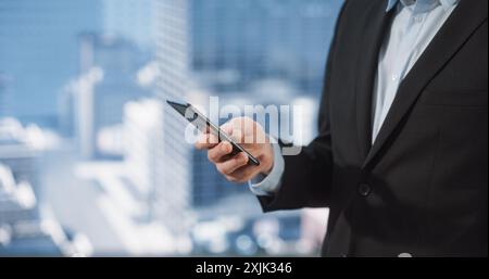 Foto ravvicinata di Entreprenuer maschile caucasico con smartphone nell'ufficio aziendale Megapolis View. Uomo d'affari di successo che controlla e-mail, pianifica, chatta online o acquista prodotti. Foto Stock