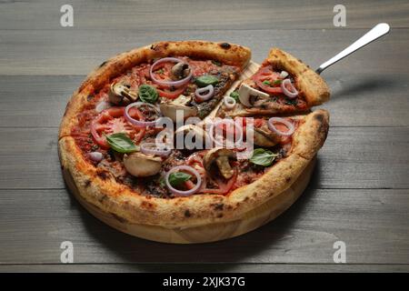 Gustosa pizza con funghi, basilico e pomodori su un tavolo di legno, primo piano Foto Stock