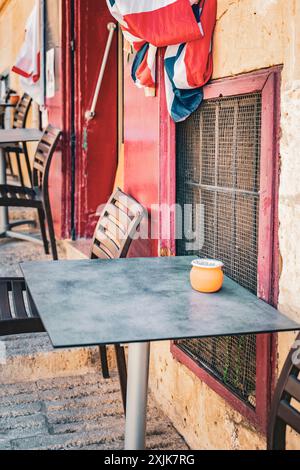 Un tavolino da caffè vuoto all'aperto con sedie con una bandiera colorata drappeggiata sullo sfondo in una giornata di sole, che evoca un senso di tranquillità e relax. Foto Stock