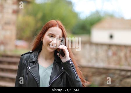 Donna con lunghi capelli rossi sorride mentre parla con il suo smartphone Foto Stock