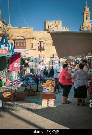 Vivace mercato all'aperto con gente che fa shopping in un villaggio mediterraneo. Bancarelle piene di prodotti colorati e prodotti locali. Edifici storici nel Foto Stock