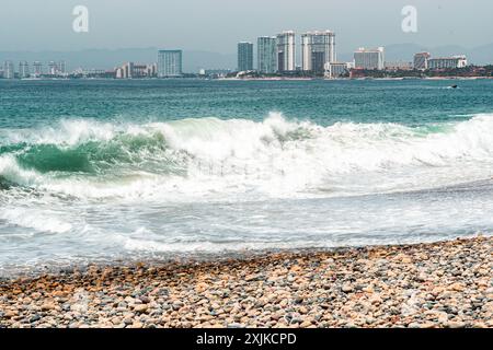 Puerto Vallarta, Messico - 27 marzo 2019: Le onde si incontrano con ciottoli sullo sfondo della città. Foto Stock