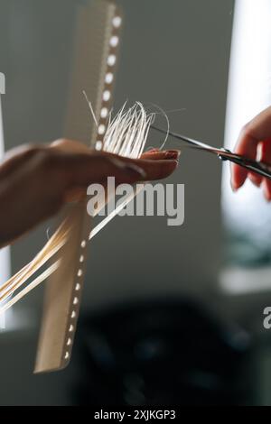 Primo piano di un parrucchiere femminile irriconoscibile che realizza un taglio elegante con forbici professionali per una donna con lunghi capelli biondi. Foto Stock